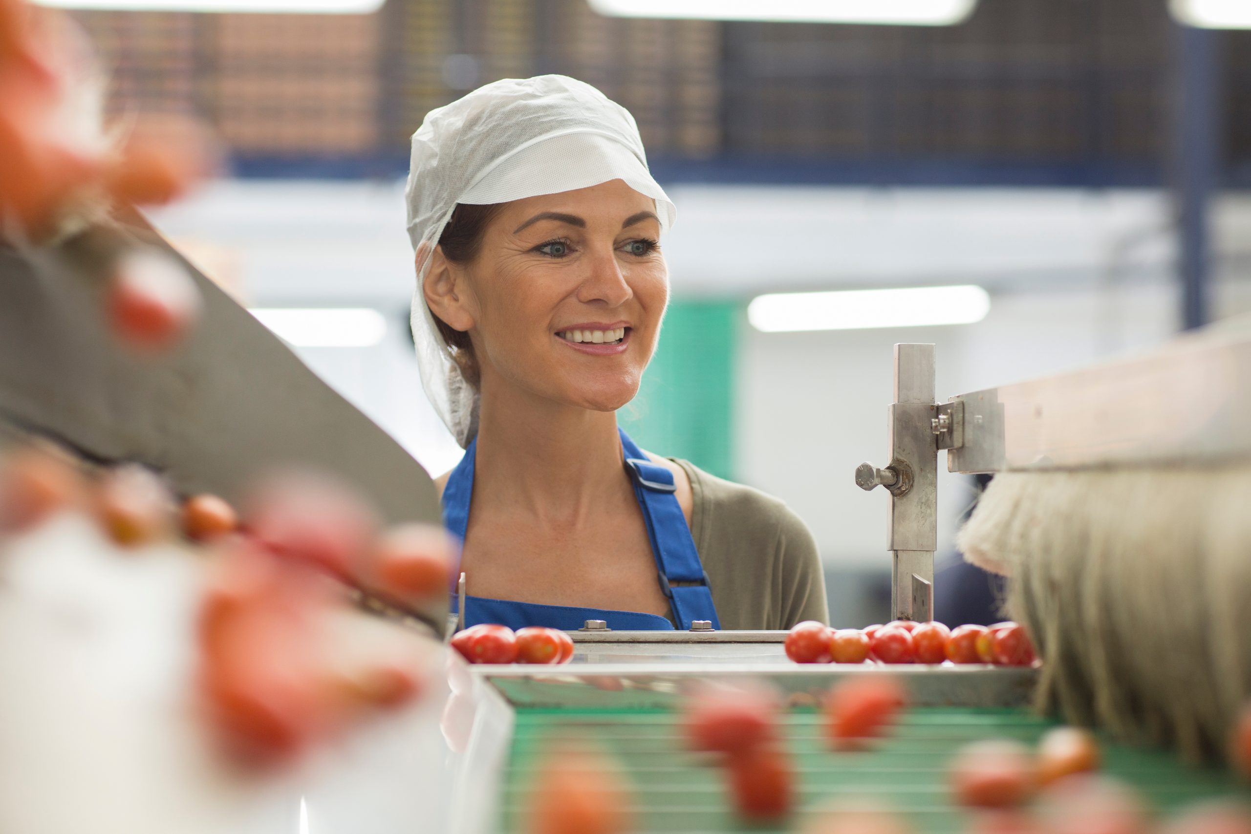 Smiling female worker watching tomatoes in food processing plant